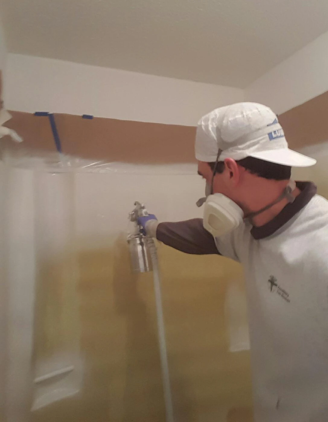 Bathtub refinishing technician in a respirator and gloves spraying new coating inside a residential bathtub during the reglazing process.